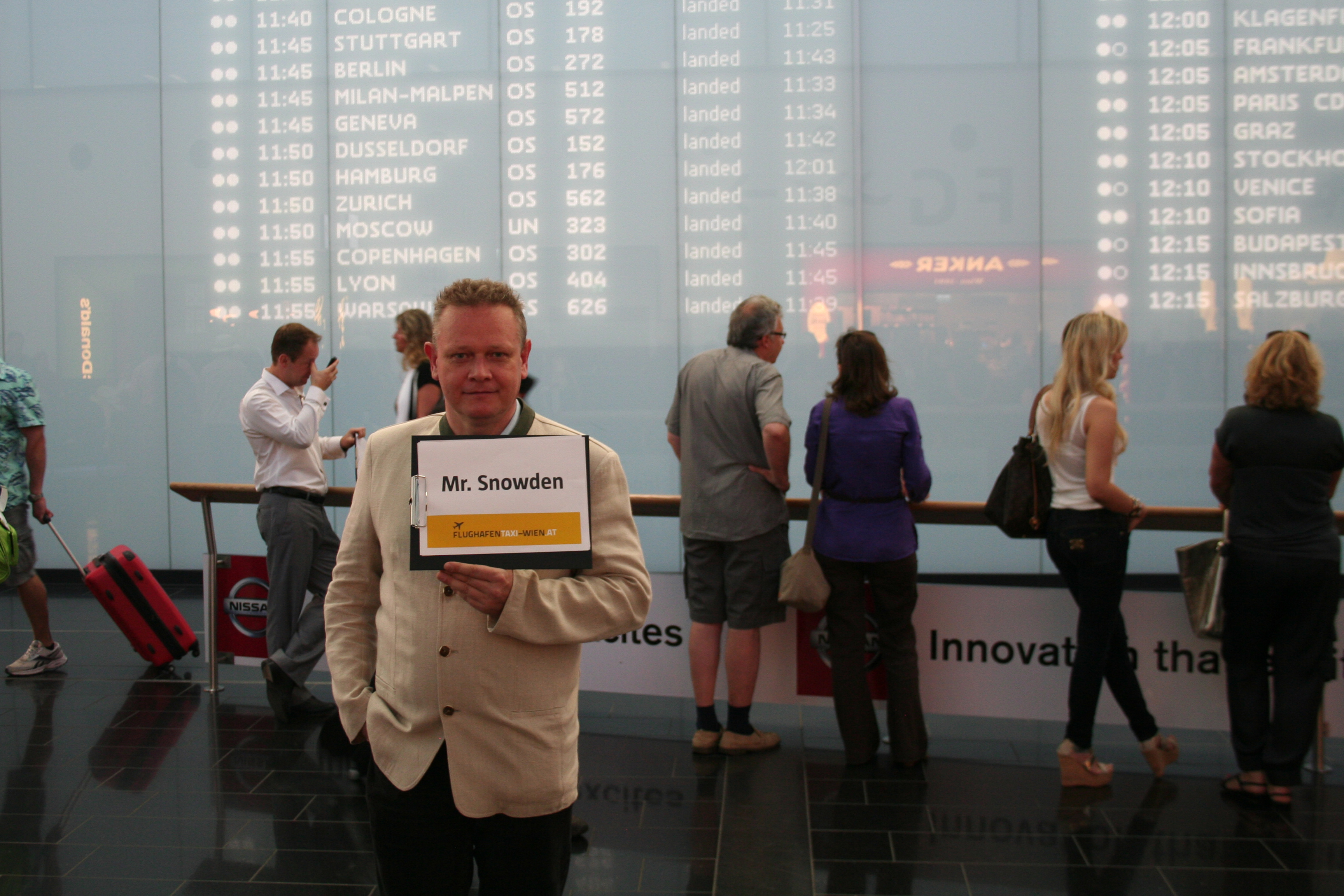 Leo Kobes als Chauffeur mit Schild "Mr. Snowden" in der Ankunftshalle des Flughafens Wien-Schwechat